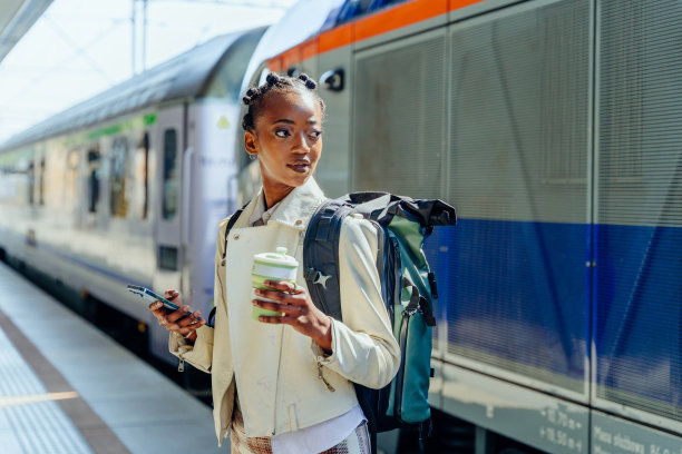 体贴的非洲年轻女子背着背包，站在火车站台上使用智能手机。图片下载