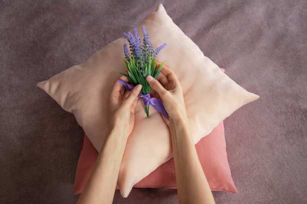 俯视图女性的手把一束薰衣草放在彩色枕头上。专业服务员用鲜花装饰床，为客人准备房间图片下载