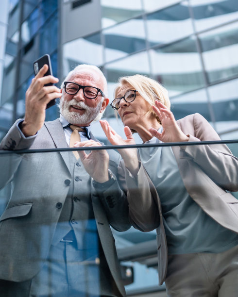 穿着西装的高级男子和成熟的金发女子作为商业伙伴，夫妻朋友或同事聊天，手里拿着智能手机浏览互联网，看照片，交换意见，复制空间图片下载