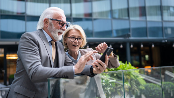 穿着西装的高级男子和成熟的金发女子作为商业伙伴，夫妻朋友或同事聊天，手里拿着智能手机浏览互联网，看照片，交换意见，复制空间图片下载
