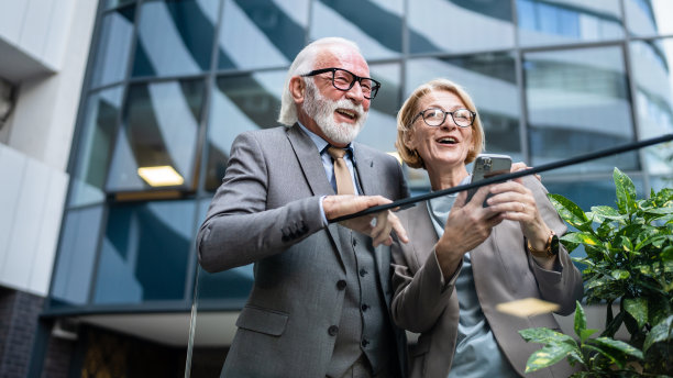 穿着西装的高级男子和成熟的金发女子作为商业伙伴，夫妻朋友或同事聊天，手里拿着智能手机浏览互联网，看照片，交换意见，复制空间图片下载