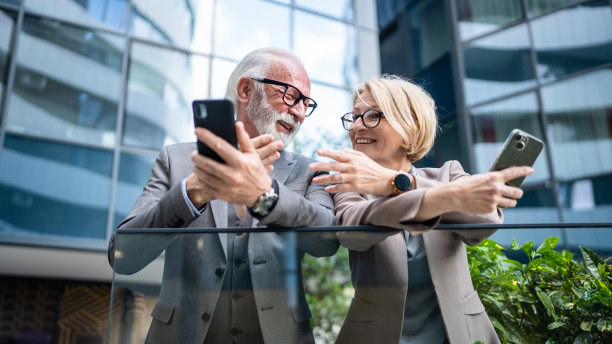 穿着西装的高级男子和成熟的金发女子作为商业伙伴，夫妻朋友或同事聊天，手里拿着智能手机浏览互联网，看照片，交换意见，复制空间图片下载