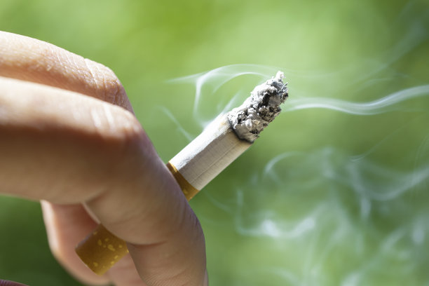 吸烟。雪茄在户外吸烟者的指间燃烧。吸烟者燃烧到最后，冒着白烟。图片下载
