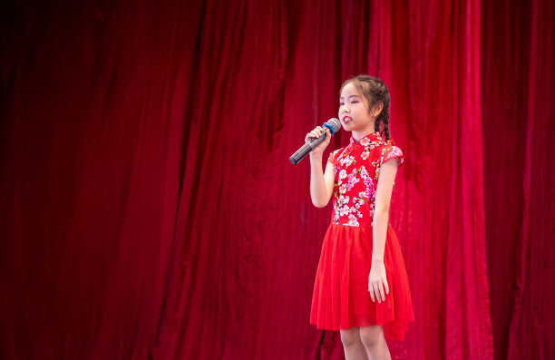 亚洲女孩在学校活动日的舞台上唱歌，穿着旗袍风格，红色窗帘背景图片下载