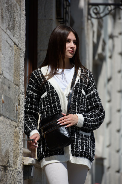 照片中的美女穿着白色紧身裤、t恤和毛衣，手里拿着一个黑色的小皮包图片下载