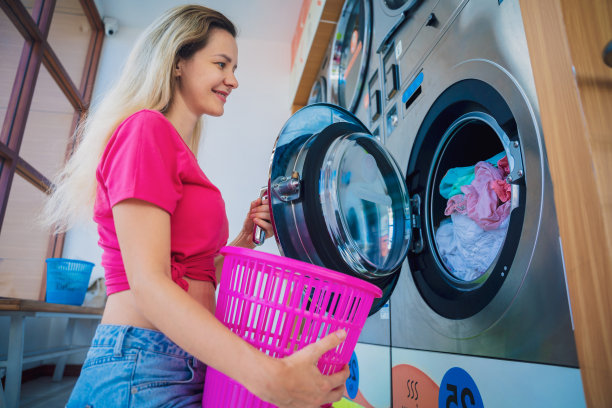年轻漂亮的女人在洗衣房洗衣服和烘干衣服图片下载