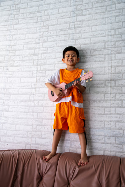 一个快乐的男孩在家里的房间里弹着原声吉他。图片下载