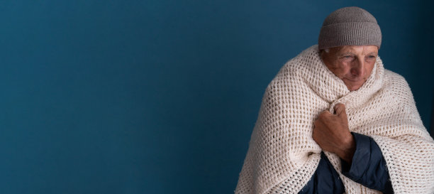 老人的肖像，在蓝色的背景在家里冻在冬天。老人戴着帽子，裹着毯子，忍受着低温，屋里的恒温器坏了图片下载