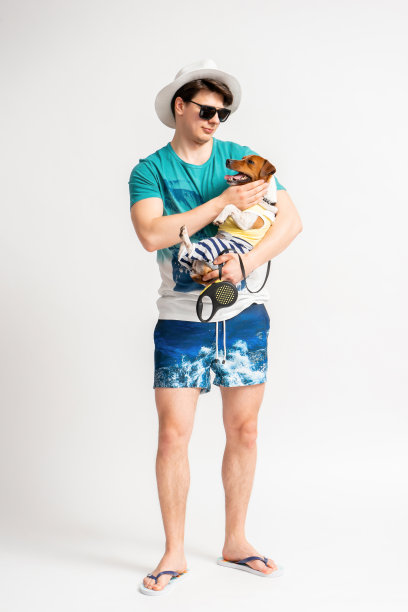 一个穿着沙滩装和人字拖的男人，怀里抱着一只杰克罗素梗犬图片下载
