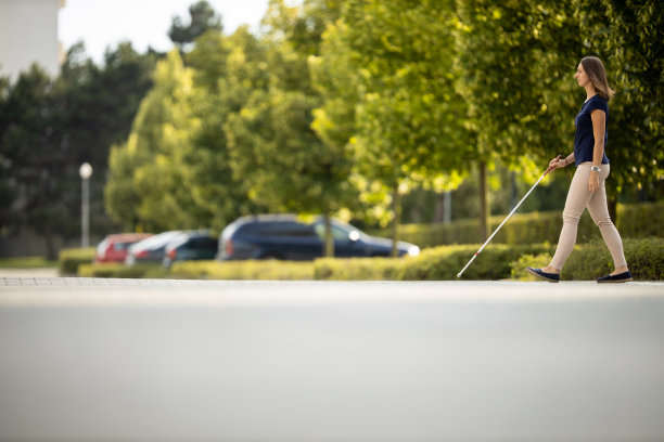 盲人妇女拄着白色拐杖走在城市街道上图片下载