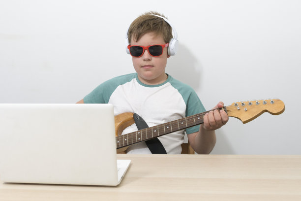 在线学习弹电子吉他。一个手里拿着吉他的男孩在电脑上观看训练节目图片下载