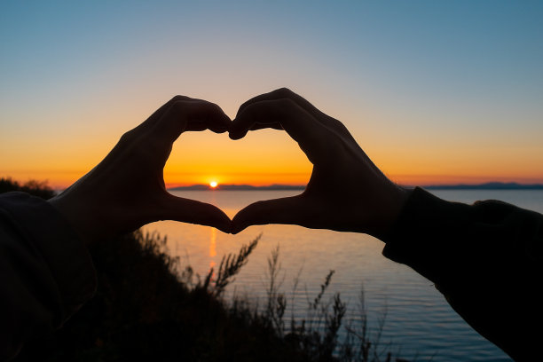 一对相爱的情侣的手在一个心形的形状，在傍晚的海边散步。图片下载