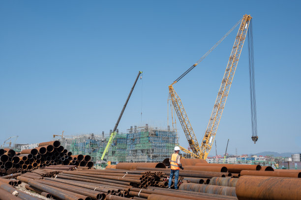化工工地上的一堆大型钢管和正在工作的起重机图片下载