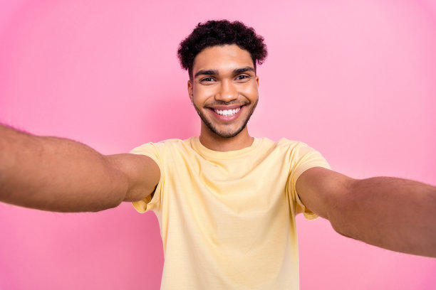 照片中，一个英俊开朗的家伙穿着时尚的黄色t恤，在粉红色的背景下为博客制作自拍视频图片下载