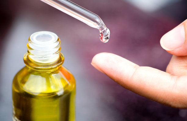 一个美丽女人的手将面部的胶原蛋白精华液滴入清澈的黄色瓶子中。护肤护理面部精华油，维生素c美容水疗概念图片下载