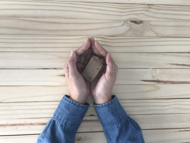 穿着蓝色牛仔裤衬衫的女人手里拿着一个棕色的小陶瓷房子图片下载