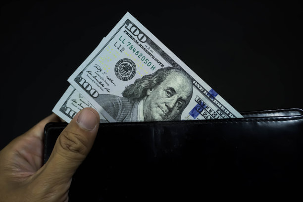 有人手里拿着两张一百元一百元的钞票，里面是黑色的长钱包，孤立在黑色的暗底上图片下载