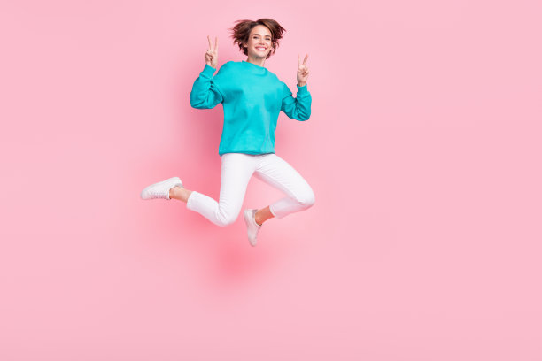 漂亮的年轻女孩的全尺寸照片显示v字跳跃飞行活动穿着时髦的蓝色服装孤立的粉红色背景图片下载