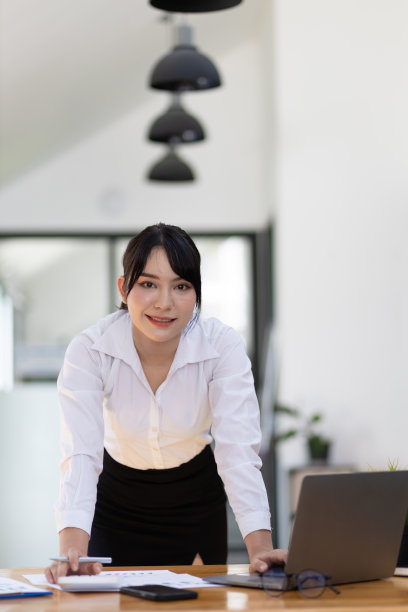 迷人的亚洲女商人的肖像，在办公桌上用笔记本电脑和文件工作。图片下载