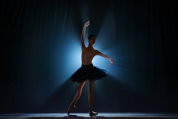 优雅的年轻女孩的优雅剪影，芭蕾舞演员在舞台上跳舞，背景是深蓝色的聚光灯图片下载