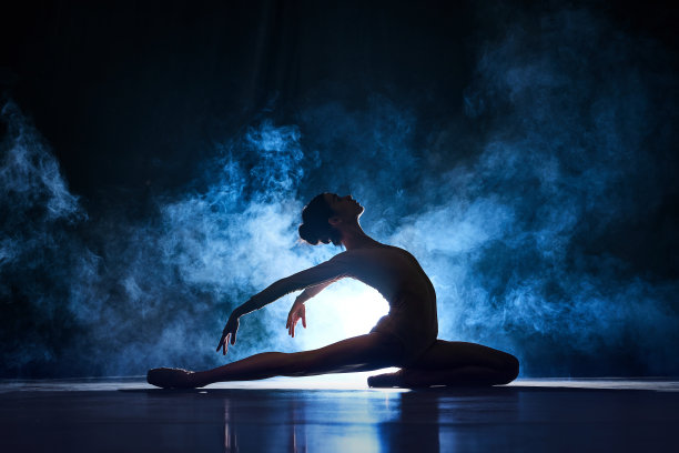 优雅，美丽，优雅的年轻女子，芭蕾舞演员在深蓝色的背景下表演与烟雾的聚光灯图片下载