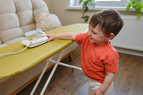 危险潜伏在房子的客厅里，一个无人看管的孩子和婴儿手中的热熨斗可能导致烧伤或受伤。两岁左右(一岁十个月)图片下载