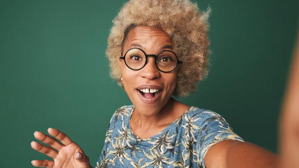 一个戴着眼镜，穿着蓝色t恤，微笑着的女孩的特写，看着相机，自拍，挥手打招呼，孤立在绿蓝色的背景下图片下载