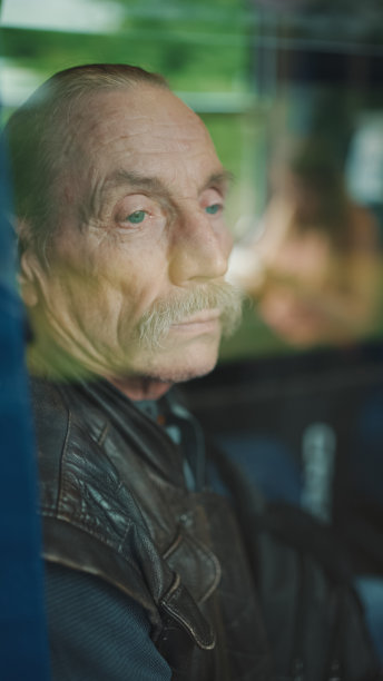 在火车车厢里旅行时，沉思的老人看着窗外，透过玻璃观看图片下载