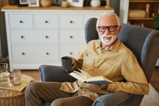 老人坐在家里的扶手椅上看书图片下载