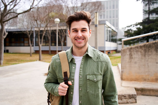 一个年轻的男学生站起来看着镜头的肖像。男人微笑着，拿着一个背包图片下载