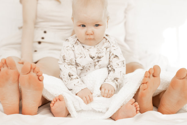 年轻的父母和小宝宝坐在床上，特写镜头图片下载