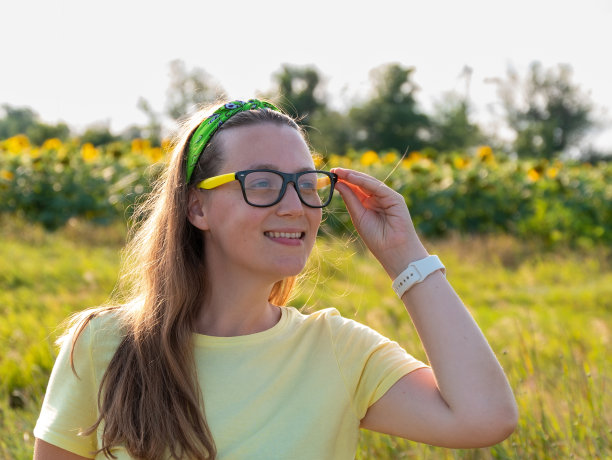 阳光明媚的向日葵田里，年轻自信的女人穿着黄色t恤。快乐真实的千禧女孩微笑户外。真实的人的生活方式照片，独自旅行，自然环境生态概念图片下载