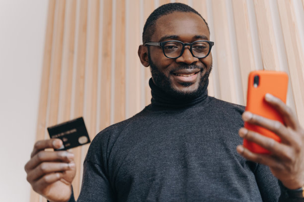 开朗的非裔美国商人，信用卡和智能手机，网上购物，开心的微笑，交易成功满意。图片下载