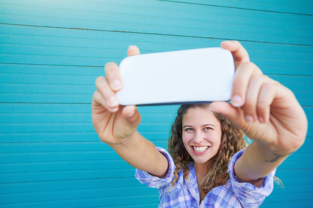 美丽的卷发年轻女子用她的手机拍了一张微笑的自拍照图片下载