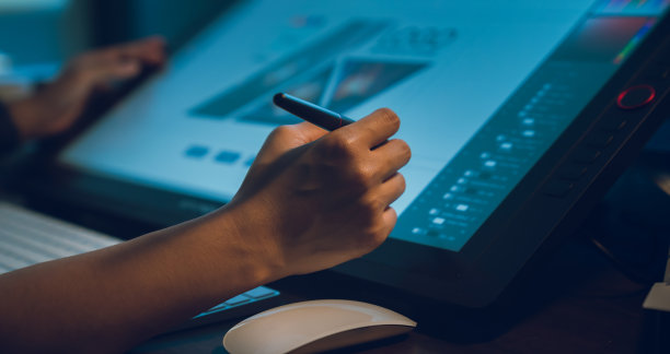 设计师在家庭工作室的桌子上工作，用数字笔在显示器屏幕上用编辑器修饰照片。图片下载