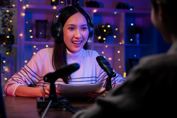 年轻的亚洲妇女使用麦克风，戴着耳机，用笔记本电脑录制播客采访电台。内容创造者概念。图片下载