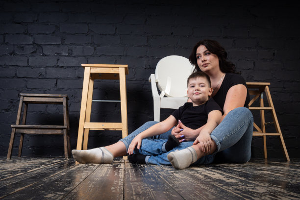 一位身穿黑色连衣裙的母亲抱着她的儿子，坐在一张高椅子上。图片下载