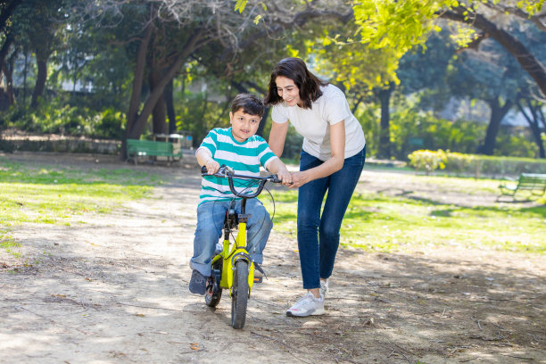 一位印度妈妈在公园里教她的儿子学骑自行车。孩子骑自行车玩得很开心，妈妈帮他保持平衡。图片下载