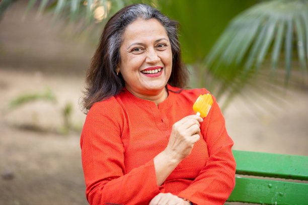 幸福的印度老年妇女在公园户外吃冰棍或冰淇淋的肖像，年长的成熟女士享受退休生活。暑假。有选择性的重点,图片下载