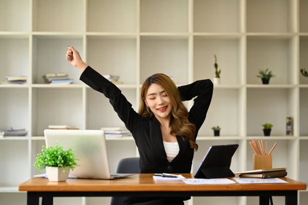 满意的女商人伸伸胳膊，在笔记本电脑前休息。缓解工作场所疲劳的概念。图片下载