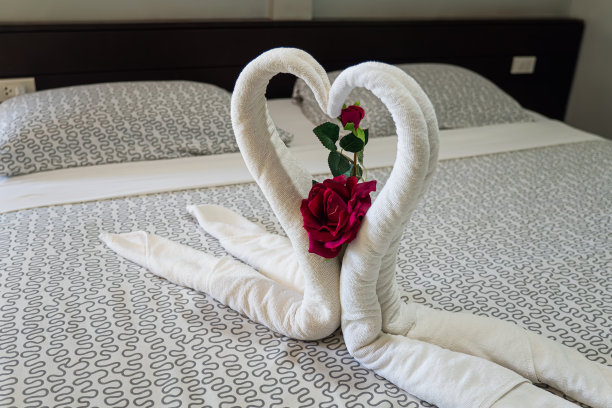 两只用毛巾做成的天鹅在蜜月床上接吻。奶油色枕头和心形图案，用红玫瑰做成的情人节签名放在卧室的床上装饰。情人节的背景。蜂蜜月亮图片下载