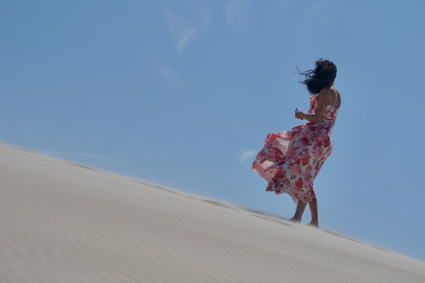 沙漠里一个穿着飘动的粉色裙子的女孩。一个女孩在晴朗的天气里走过沙漠。沙漠里美丽苗条的女孩。沙漠中的模特。一个女孩在刮风的日子里走在沙丘的沙滩上。图片下载