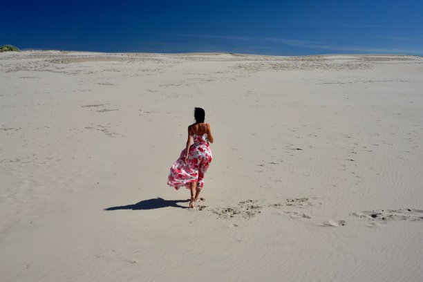 沙漠里一个穿着飘动的粉色裙子的女孩。一个女孩在晴朗的天气里走过沙漠。沙漠里美丽苗条的女孩。沙漠中的模特。一个女孩在刮风的日子里走在沙丘的沙滩上。图片下载