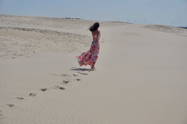 沙漠里一个穿着飘动的粉色裙子的女孩。一个女孩在晴朗的天气里走过沙漠。沙漠里美丽苗条的女孩。沙漠中的模特。一个女孩在刮风的日子里走在沙丘的沙滩上。图片下载