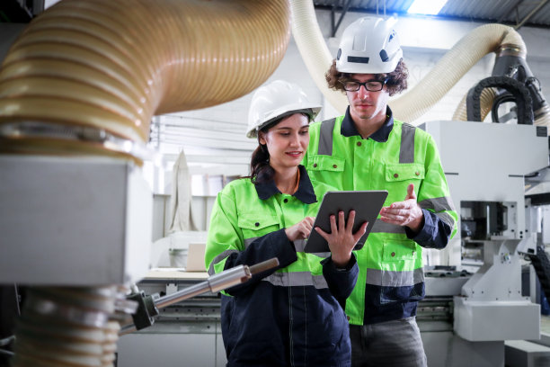 快乐的工业男女工人戴着头盔和安全背心，在家具厂与自动机器人机械一起工作，男女技术员检查平板电脑，数控木工。图片下载