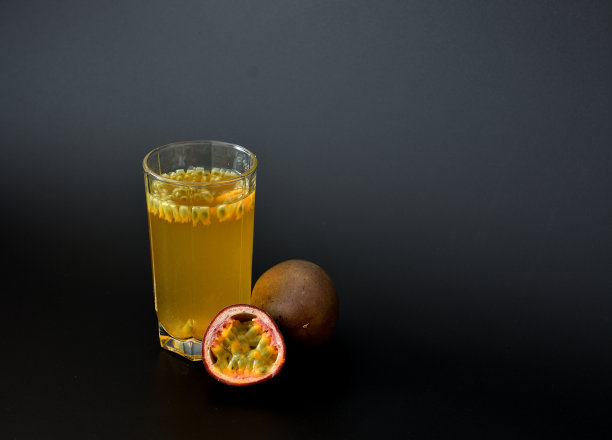 一杯黑色背景的新鲜果汁，旁边是成熟的百香果。图片下载