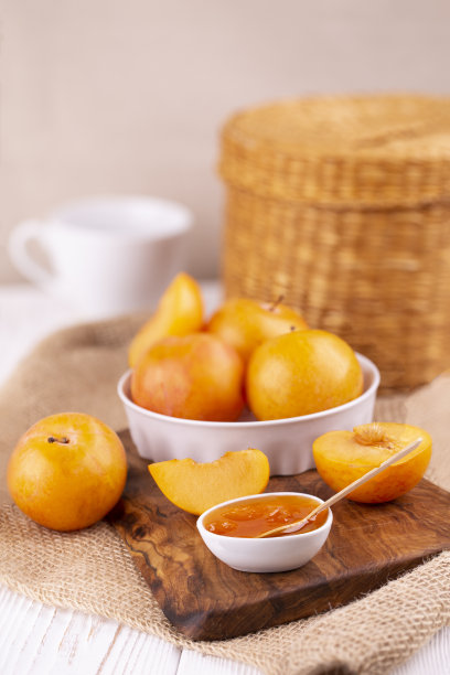 在舒适明亮的厨房里，白色碗里盛着梅酱，木板上的黄梅整片整片的特写，垂直照片。图片下载