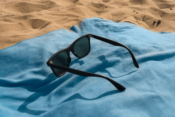 太阳镜在蓝色布料和沙滩上的侧视图图片下载