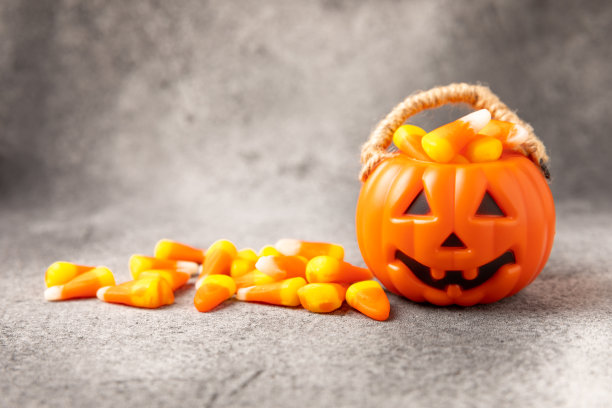 背景是玉米糖。万圣节的概念。一桶万圣节南瓜南瓜灯和玉米糖庆祝万圣节。南瓜脸上带着可怕的微笑。糖果桶。图片下载