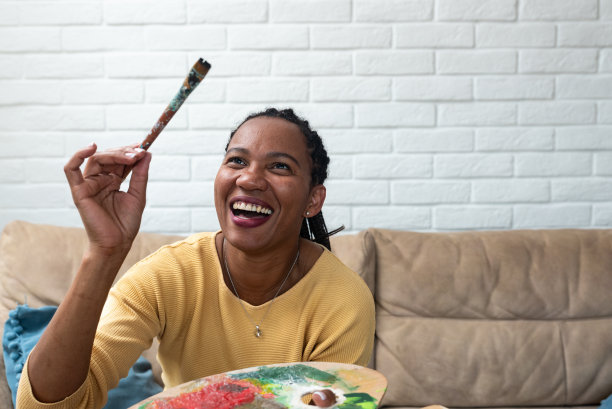 非裔美国女艺术家在艺术工作室自信地微笑着画画。女画家用画笔和色彩绘画艺术，为展览做准备，享受创作。图片下载